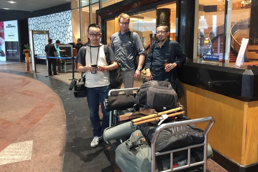 Lipson, Wu and Guilianno with trolley loaded with gear outside hotel.