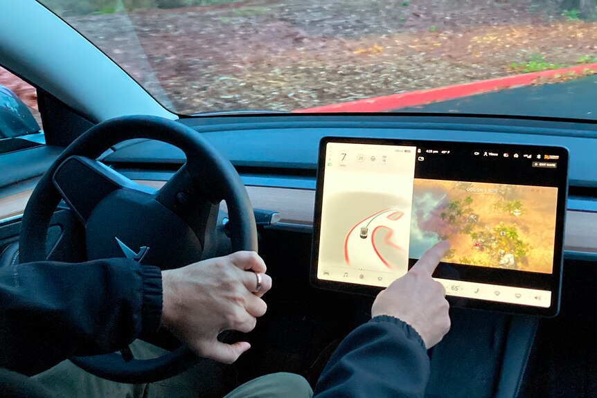 A driver demonstrates playing a game on a car's large centrally mounted touch screen.