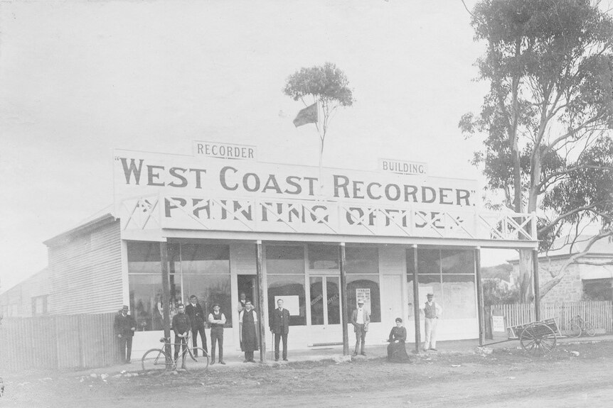An old photo with a group of people standing outside an old building where the West Coast Recorder was printed