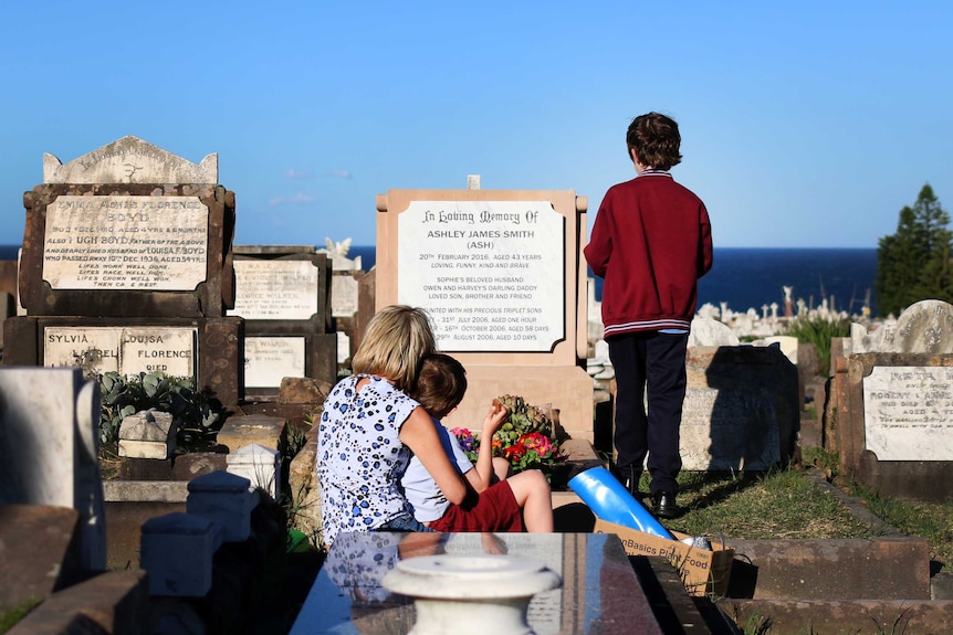 Sophie Smith hugs one of her sons while the other stands in front of a gravestone for Sophie's late husband