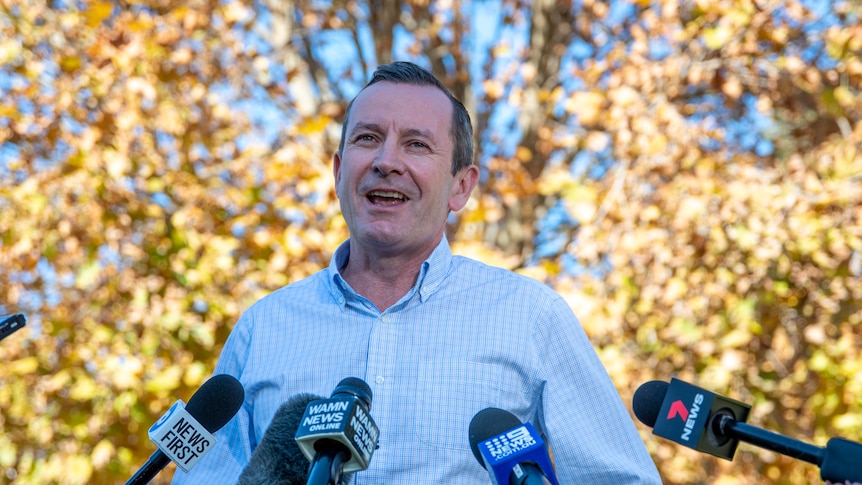Mid shot of Mark McGowan, smiling in front of several microphones. 