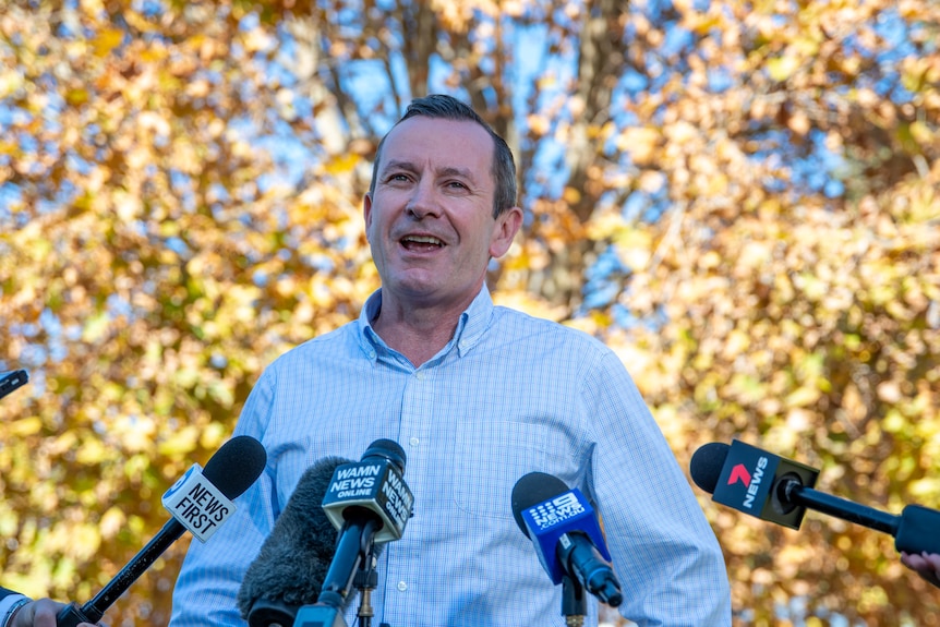 Mid shot of Mark McGowan, smiling in front of several microphones. 