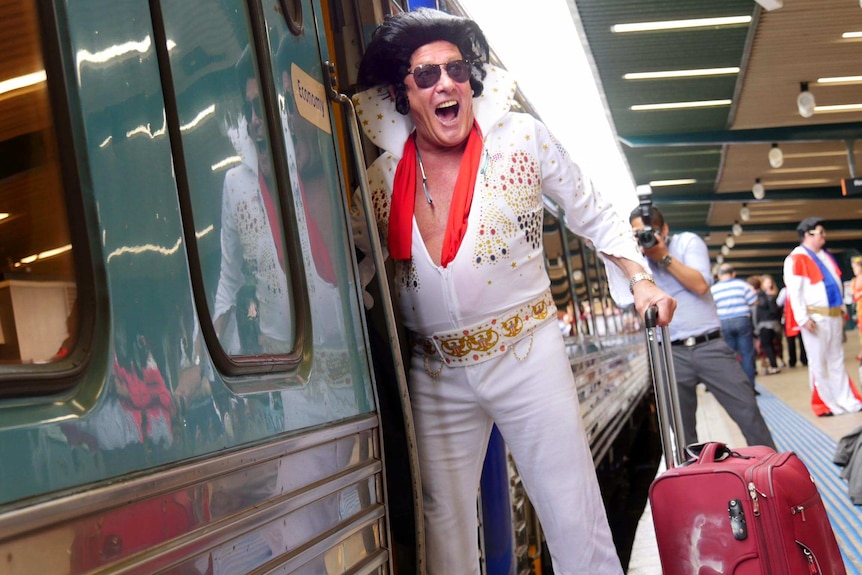 An Elvis impersonator smiles broadly as he stands in the doorway of the Elvis Express train.