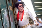 An Elvis impersonator smiles broadly as he stands in the doorway of the Elvis Express train.