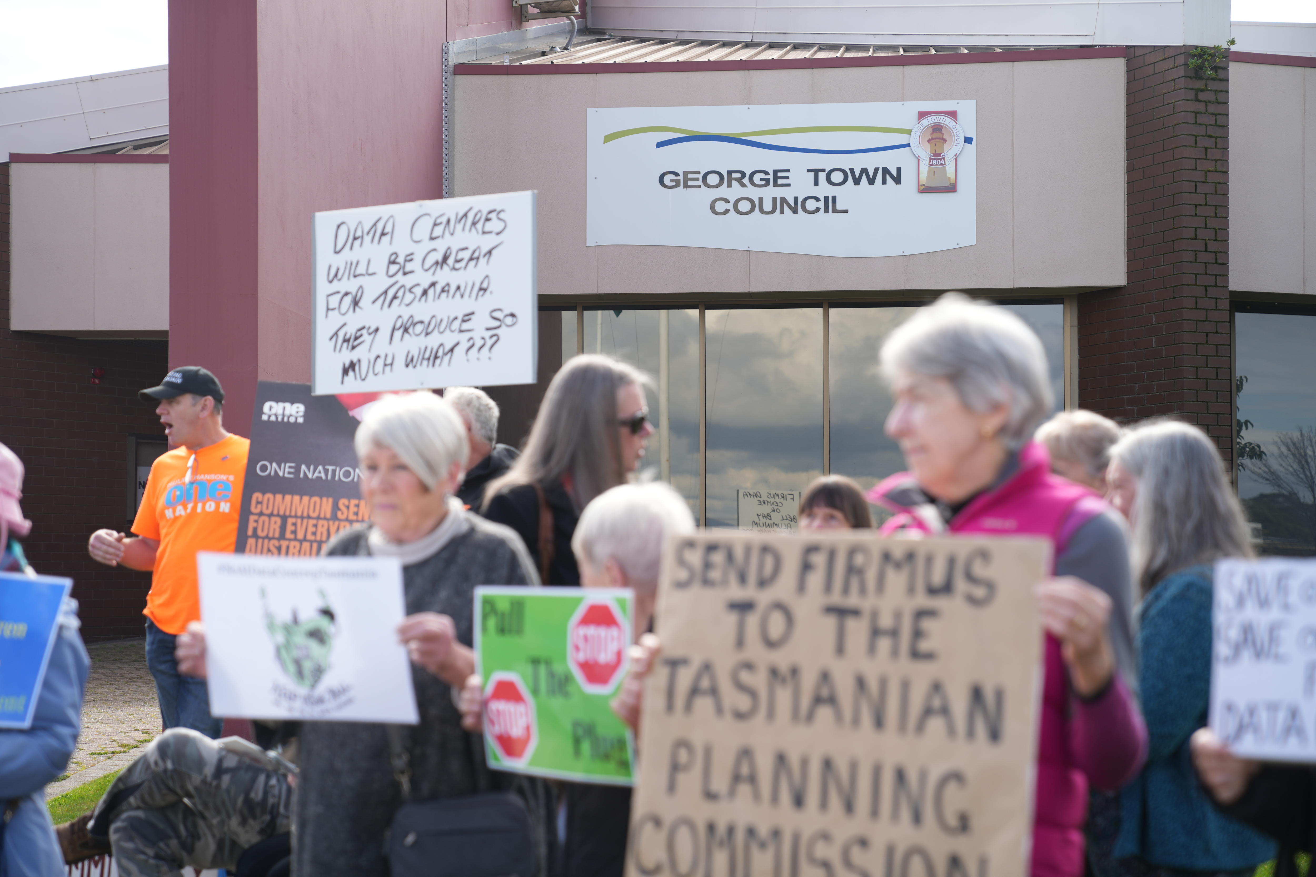 People rally outside the chambers holding signs.
