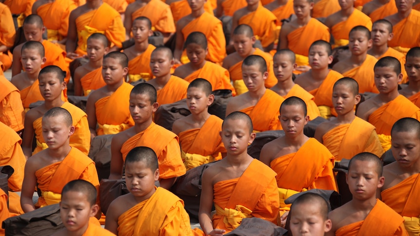 A large group of Buddhist monks wearing orange robes meditating