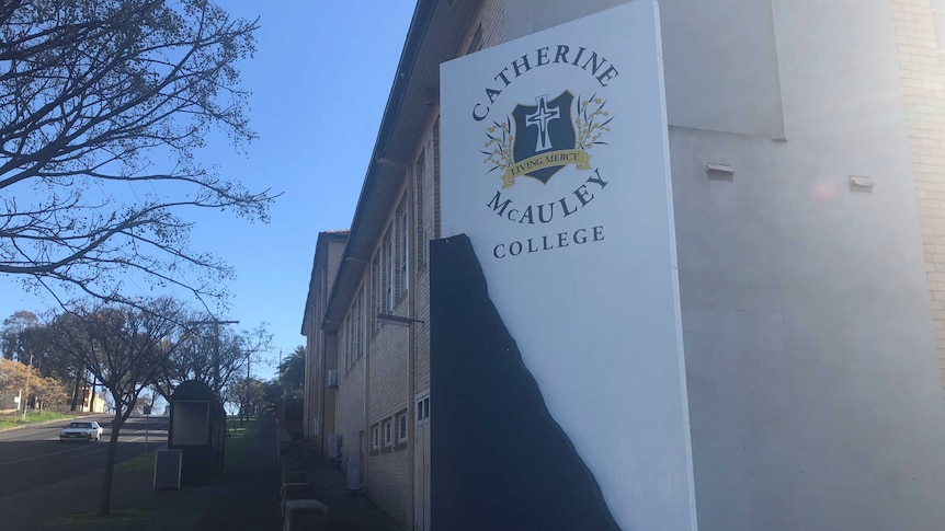 A sign with the catherine mcauley college logo sits outside the school