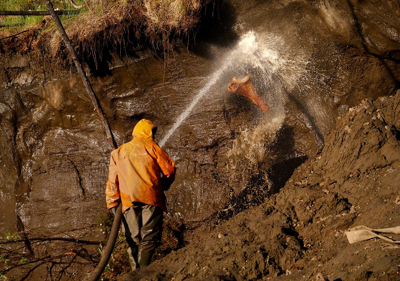 man spraying mud cliff with water