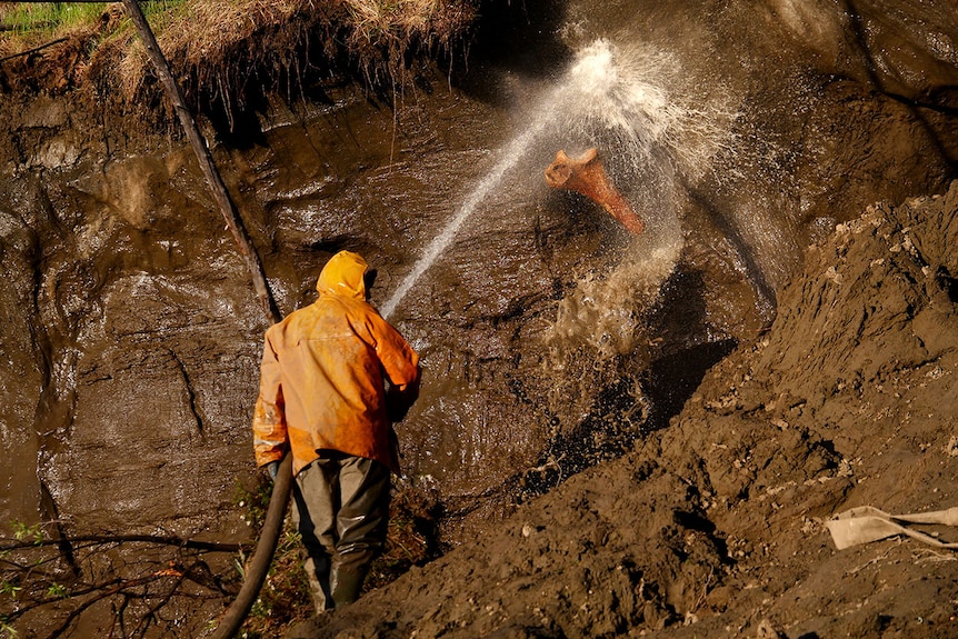 man spraying mud cliff with water