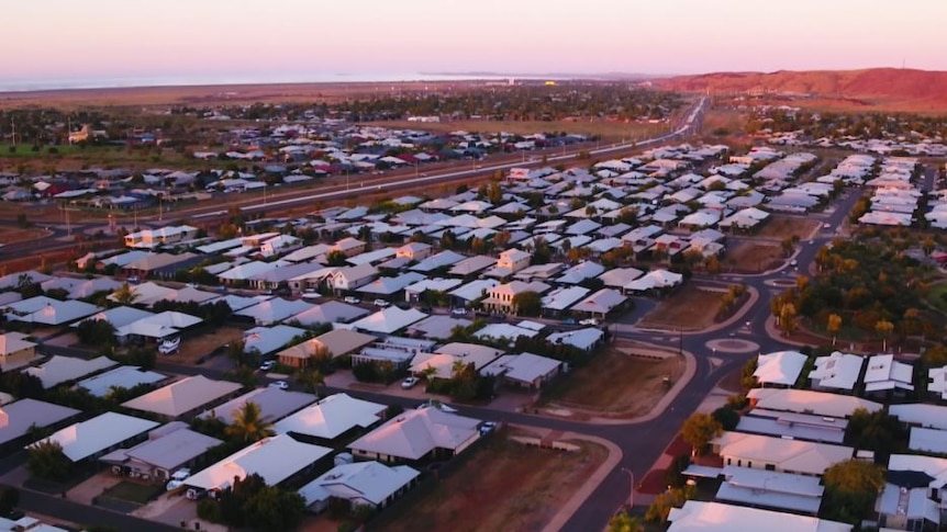 An aerial photo shows hundreds of houses in Karratha with white roofs on red dirt.