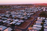 An aerial photo shows hundreds of houses in Karratha with white roofs on red dirt.