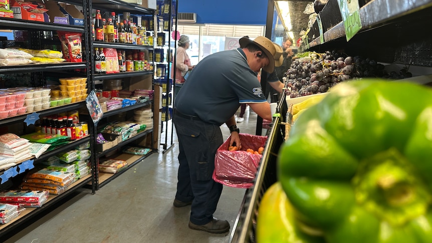 An older man in a supermarket aisle shopping for fresh fruit.