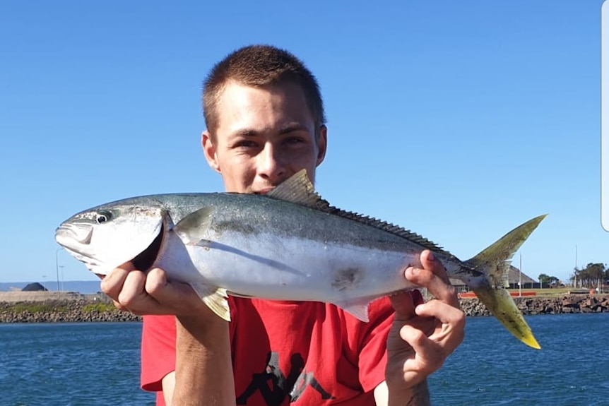 a young man holds a fish with water in the background