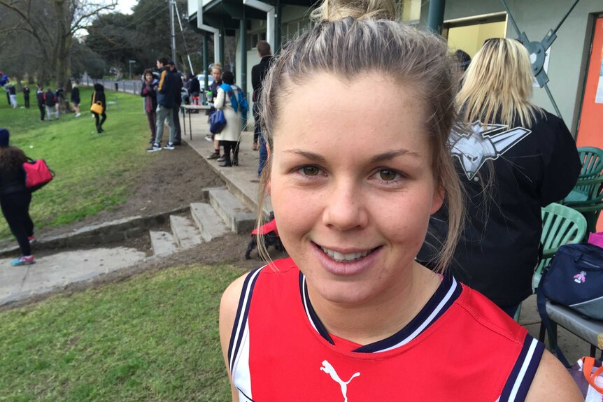 Katie Brennan in afl uniform smiling at football ground.