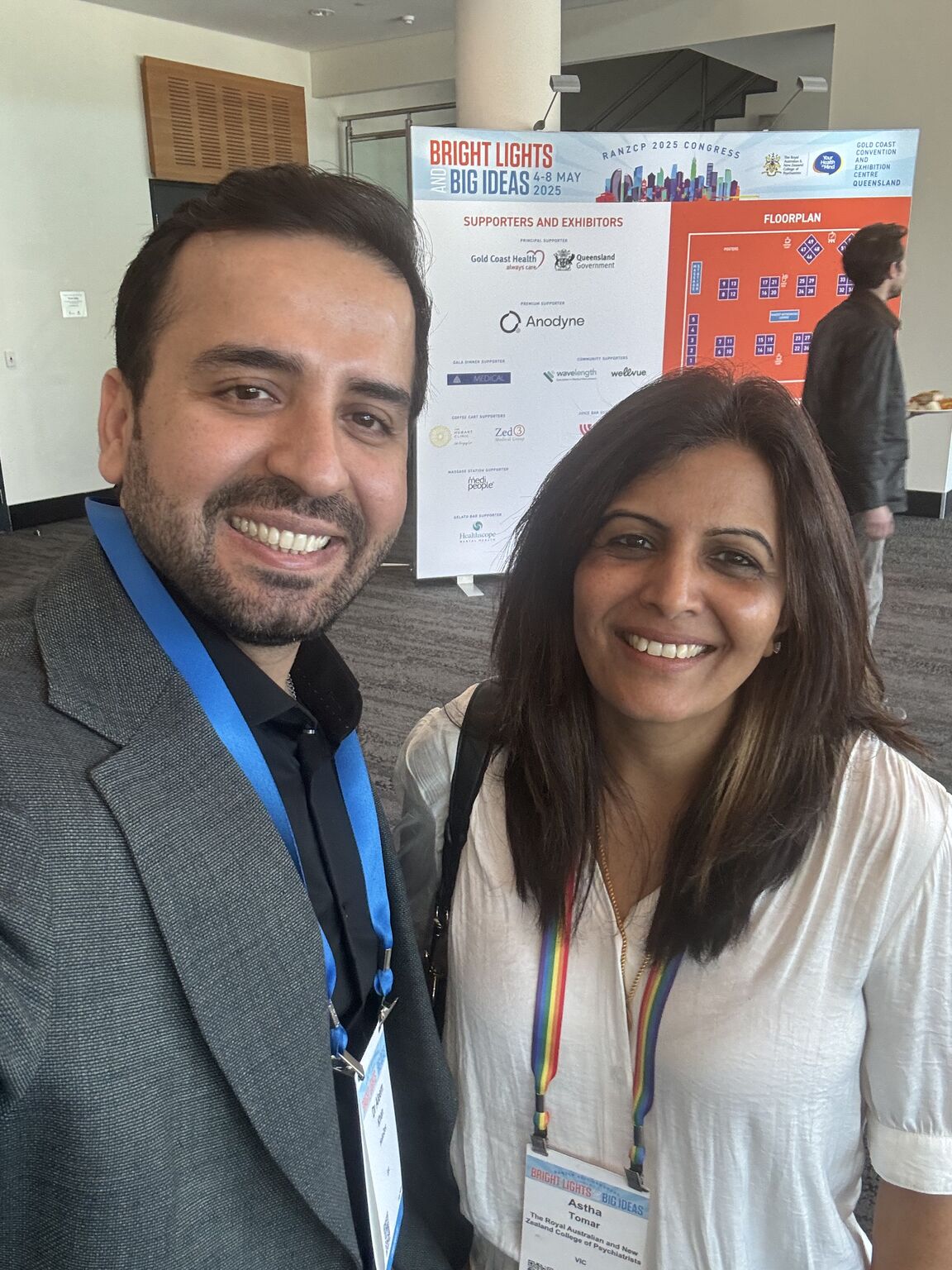 Aleem Khan on the left and  Astha Tomar on the right take a selfie indoors with a person in the background.