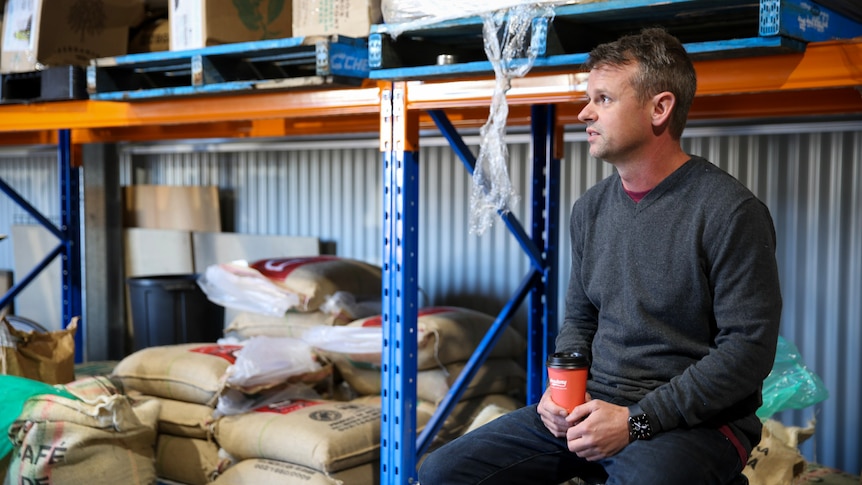 Matt Swiatkiwsky sits on chair in Academy Coffee warehouse with coffee bags in background