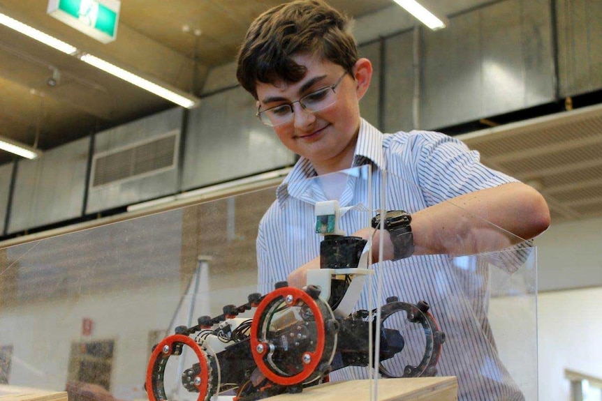 A student stands over a clear perspex box with a robot in.