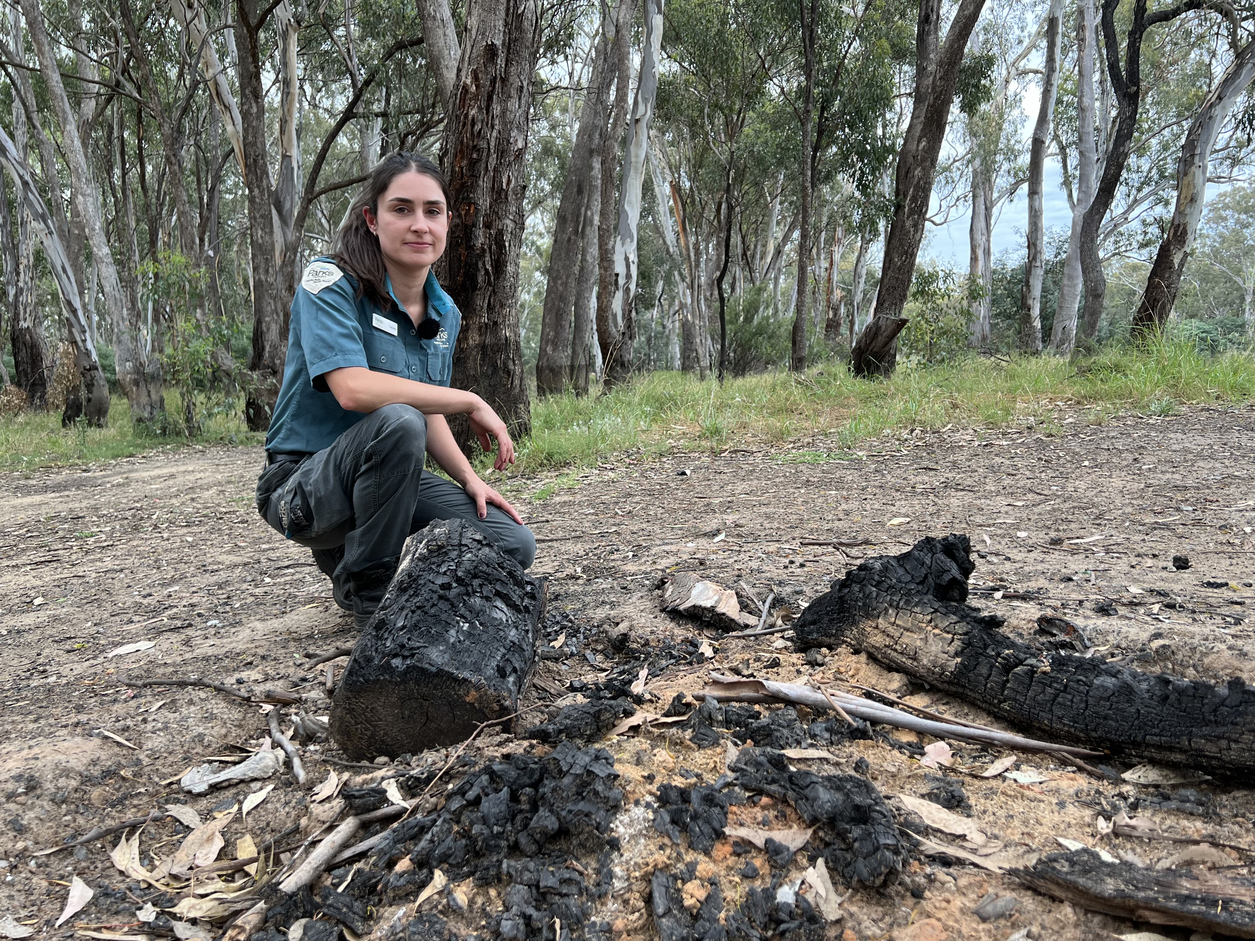 a photo of a woman in ranger uniform with dark hair crouching over burnt out fire 