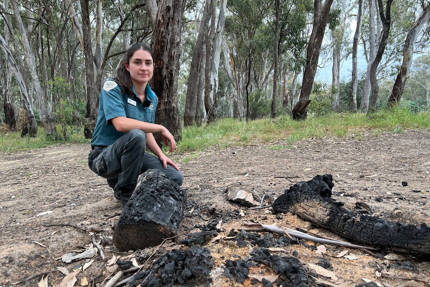 a photo of a woman in ranger uniform with dark hair crouching over burnt out fire 