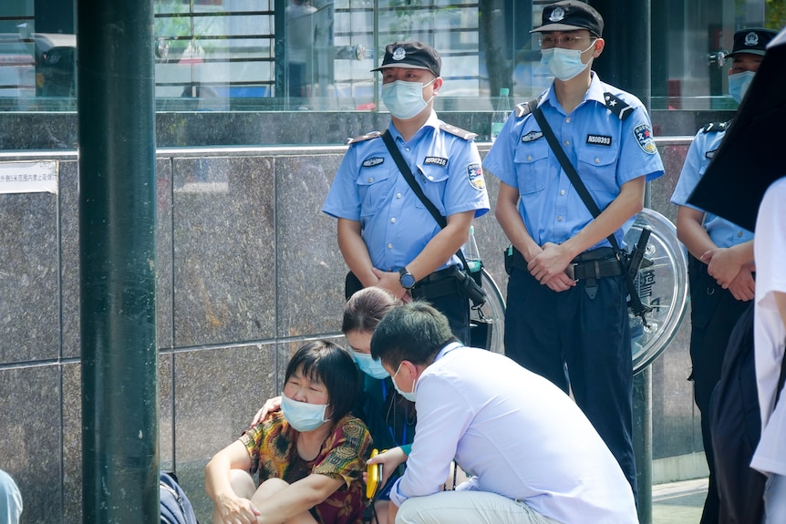A Chinese woman in a face mask sits on the floor sobbing while people crouch down to comfort her