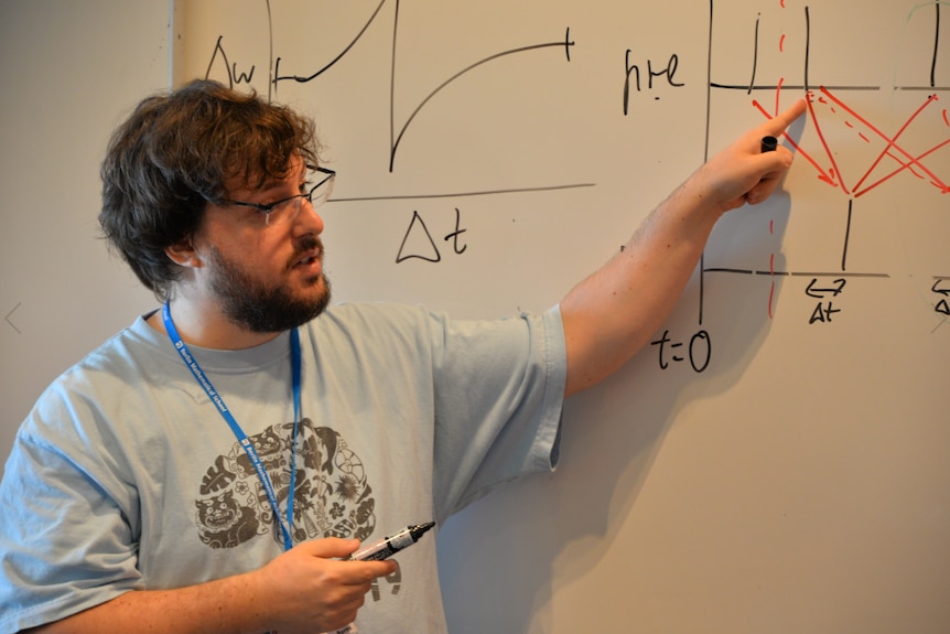 A man is pointing to a drawing on a whiteboard