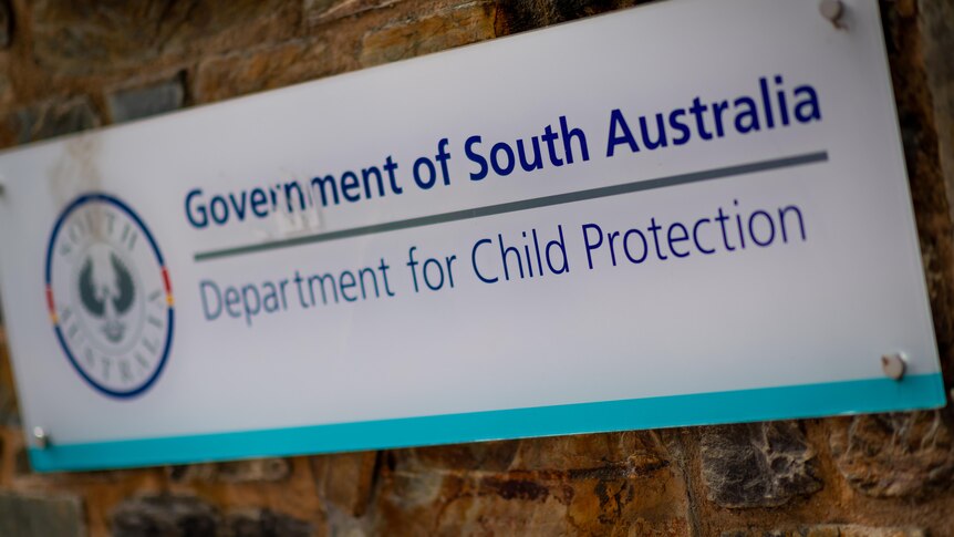 White and blue government of SA Department for Child Protection sign nailed to stone wall.