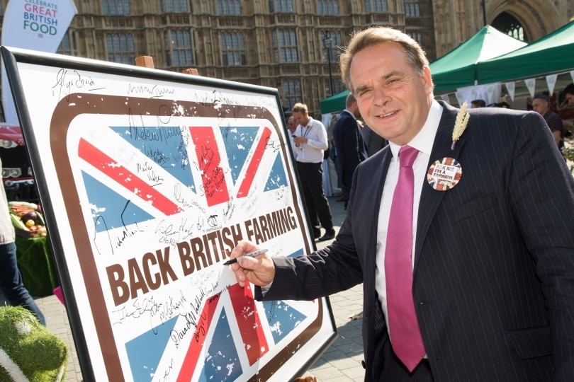 Man in a suit smiles has he signes his name on a board.