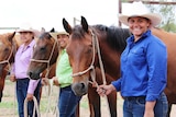 Three teenage girls holding onto horses' reins.