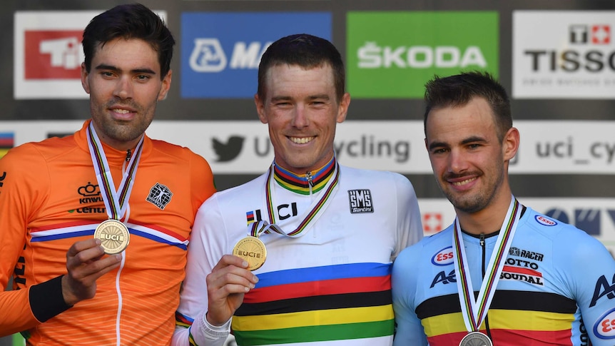 Three men stand holding medals with smiles on their faces