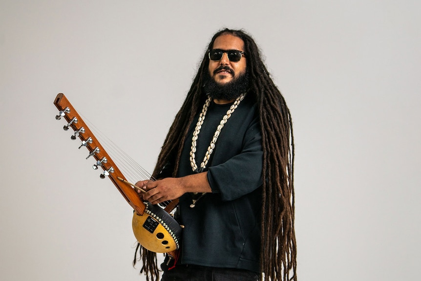 The musician Julian Bel Bachir with a string instrument, shell necklace, long dreadlocks