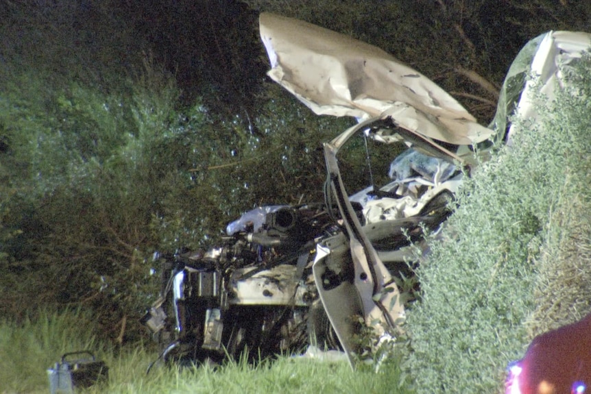 A light-coloured car left badly damaged, with its door off the hinges and the bonnet twisted metal.