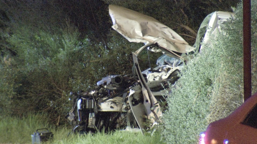 A light-coloured car left badly damaged, with its door off the hinges and the bonnet twisted metal.