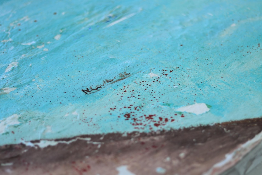 A blue painting with a signature in the middle of the shot.