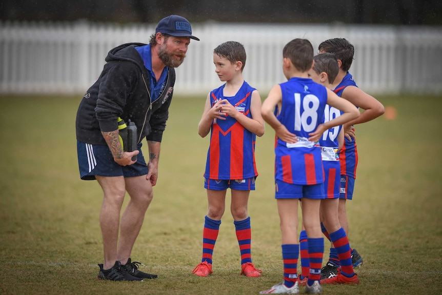 A man with a beard speaks to junior Aussie rules players.