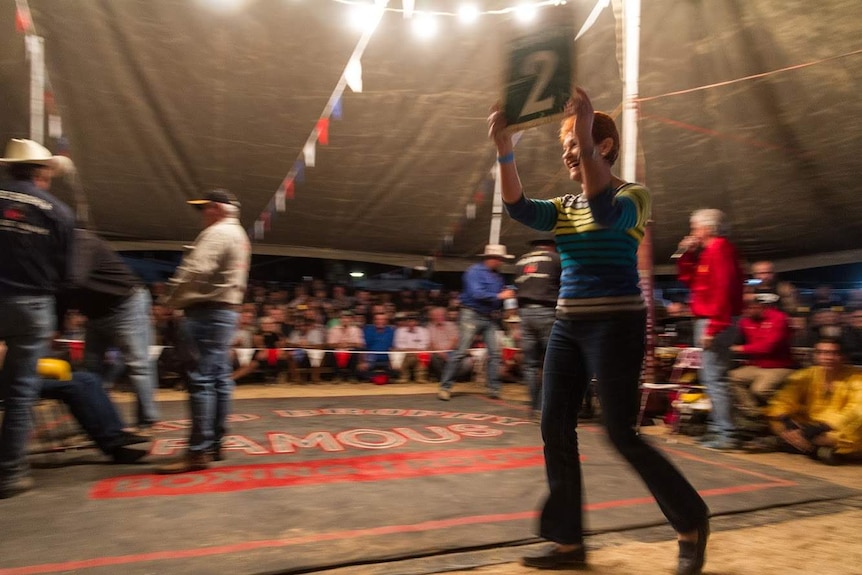 Pauline Hanson holds up a sign with the number 2 on it on a boxing ring under the big tent.