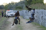 Hungarian police watch as Syrian migrants climb under a fence to enter the country