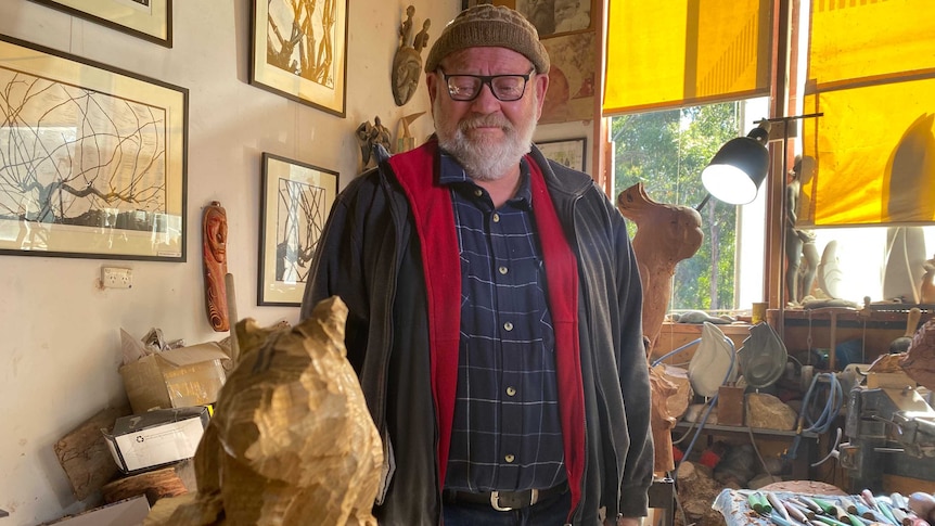 A man wearing a beanie looking at a wood carving of a wombat