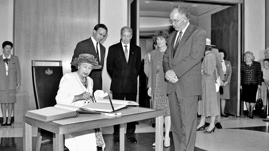 Queen Elizabeth II signs the visitors' book at Parliament House, as Paul Keating and officials watch on.