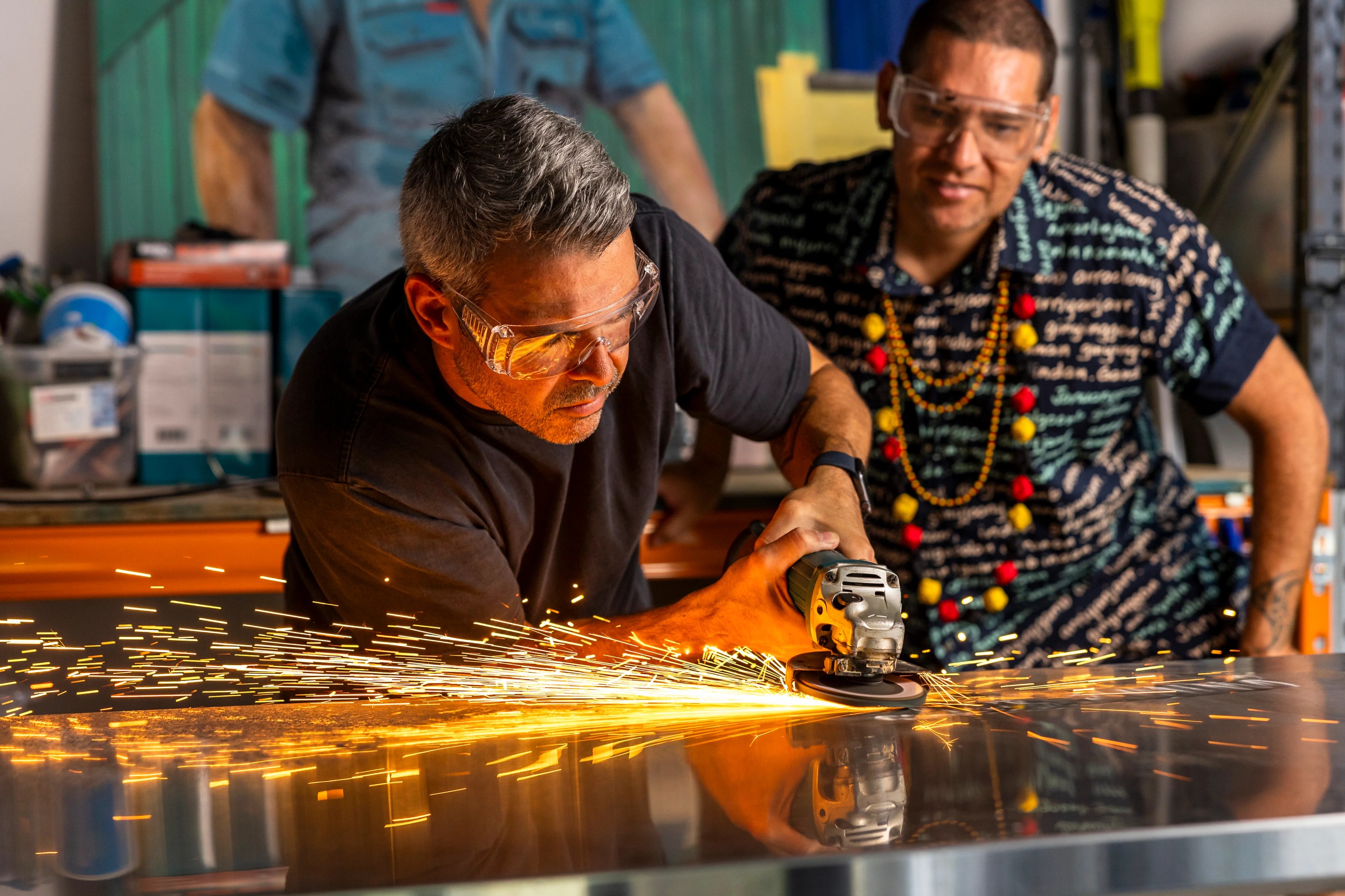 En un estudio, Warraba Weatherall, un indígena, trabaja con una máquina rectificadora de metales. Detrás de él está Tony Albert.