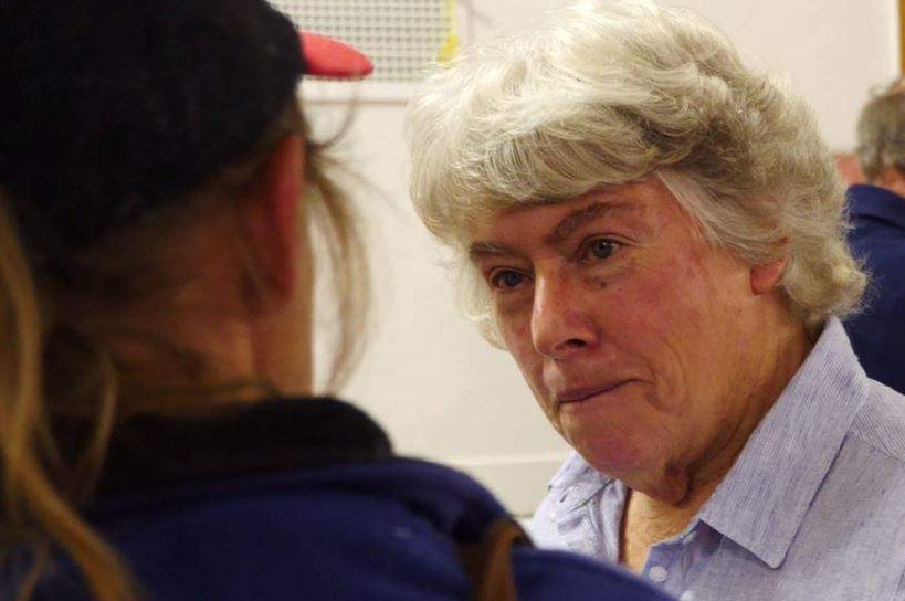 An older woman with cropped grey hair speaking to a woman wearing a baseball cap.
