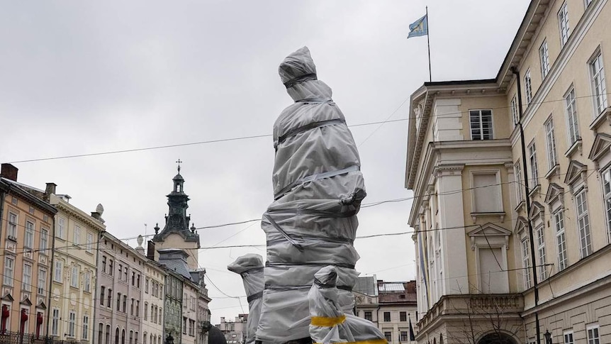 On an overcast day, a statue on a street lined by neoclassical buildings in Lviv is wrapped in plastic and taped up.