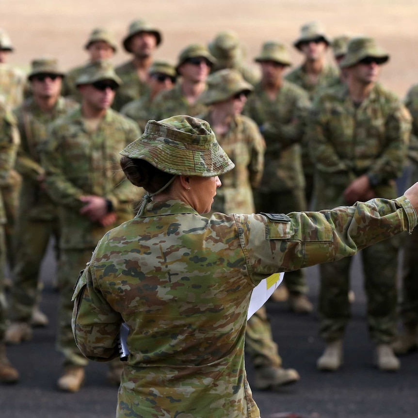 A uniformed army official is giving instructions to a group of uniformed army members.