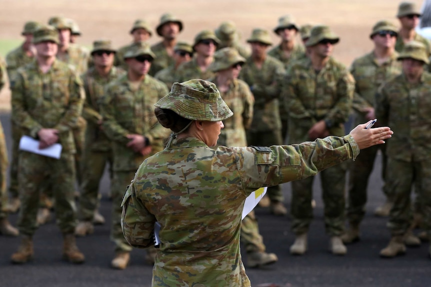 A uniformed army official is giving instructions to a group of uniformed army members.