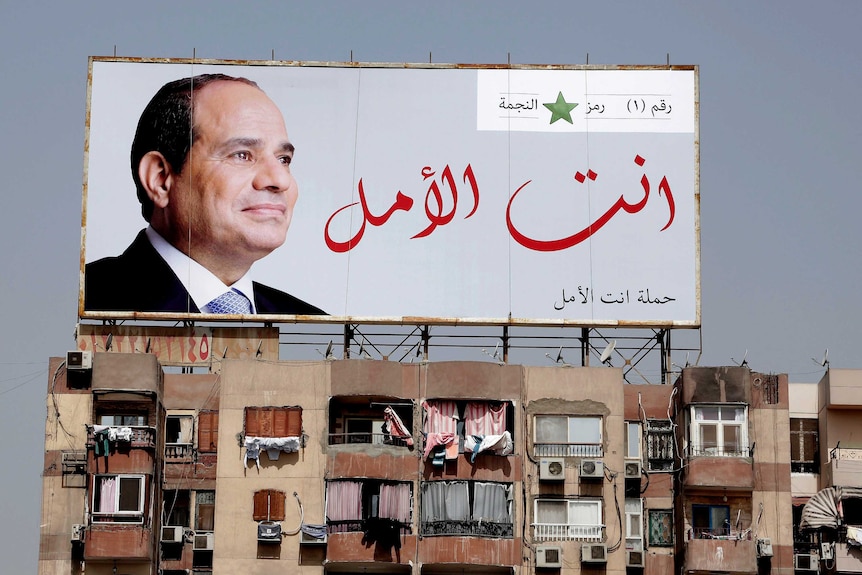 A large billboard with a big photo of Abdel Fattah el-Sisi sits on top of an apartment building.