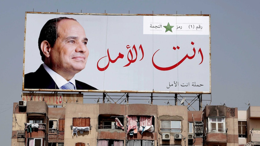 A large billboard with a big photo of Abdel Fattah el-Sisi sits on top of an apartment building.