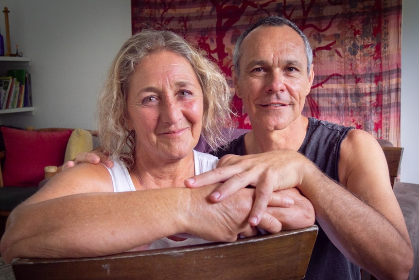 Portrait of a woman and a man together in a loungeroom looking at the camera.  He has his hand on her shoulder and arm.