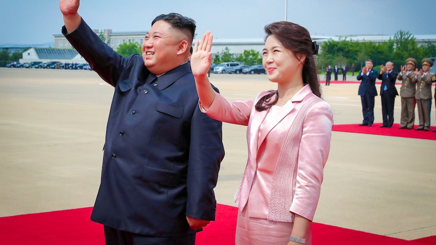 Kim Jong Un and a woman in a pink silk suit wave on an airport tarmac 