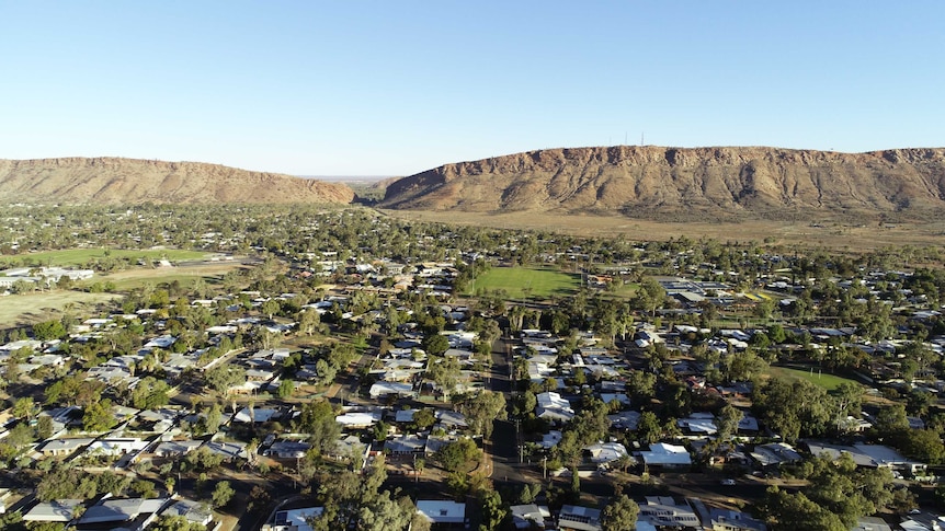 An aerial shot of an outback town – Alice Springs – in front of a mighty rock formation.