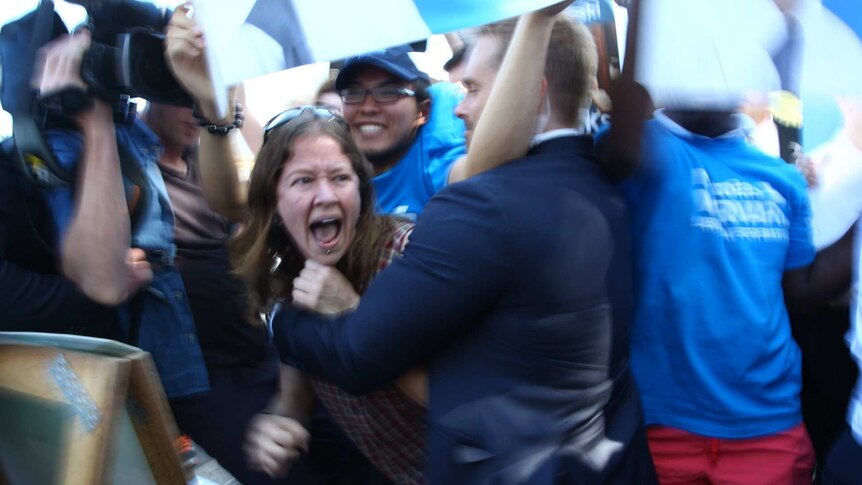 A protestor is held back by a member of Tony Abbott's security team
