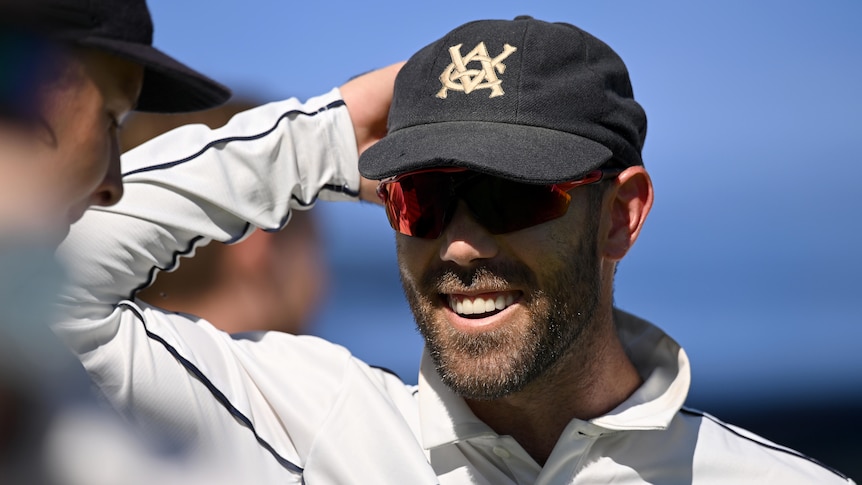 Victorian cricketer Glenn Maxwell stands with a navy blue cap on his head, smiling after a Sheffield Shield win.